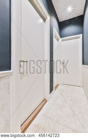 Light Narrow Hallway With Many Doors In Blu Walls And Glowing Lamp Over Lumber Floor