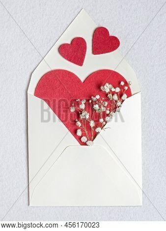 Top View Of An Open Envelope With Red Felt Heart And Dry Flowers On A White Felt Background. Romanti