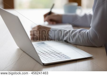 Unknown Woman Sit At Desk With Laptop Jotting On Paper