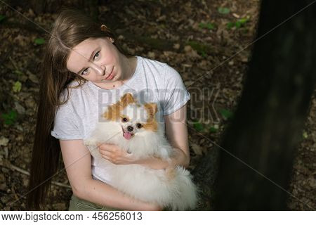 Young Woman With Long Straight Hair And Fluffy Small Dog For Walk In Forest.