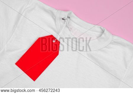 Blank Red Price Tag On White T-shirt. White T-shirt On A Pink Background With A Red Blank Label