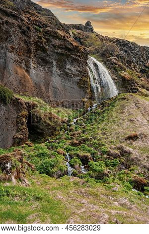Beautiful Gljufrabui Waterfall Flowing From Mountain Against Cloudy Sky At Sunset
