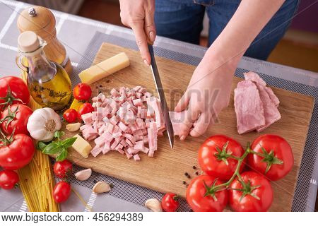 Womans Hands Slicing Pancetta Ham Bacon On Wooden Cutting Board At Domestic Kitchen