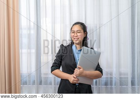 Laptop In Asian Woman\'s Hand, Stands In Front Of Window At Private Bedroom