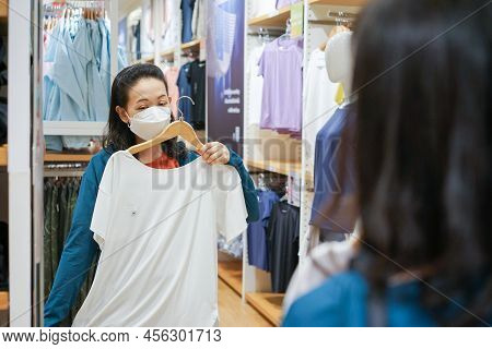 Young Asian Woman Try Size T Shirt In Front Of The Mirror In Cloth Fashion Shop.