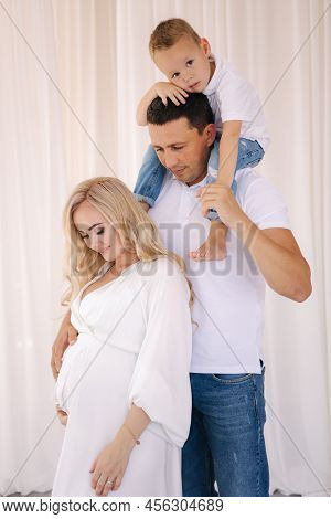 Dad Hold His Son On Neck And Hug His Pregnat Wife. Family Look Concept For Studio Photosession. Pere