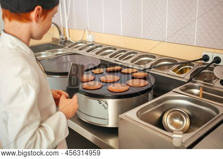 Boy Cooks Pancakes On An Industrial Professional Pancake Maker, Kitchen In Cafe, Little Chef. Flips 