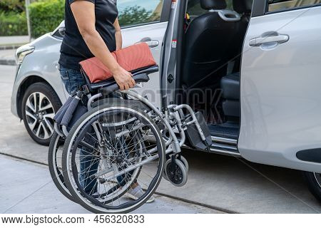 Asian Woman Folding And Lift Up Wheelchair Into Her Car. Accessibility Concept.