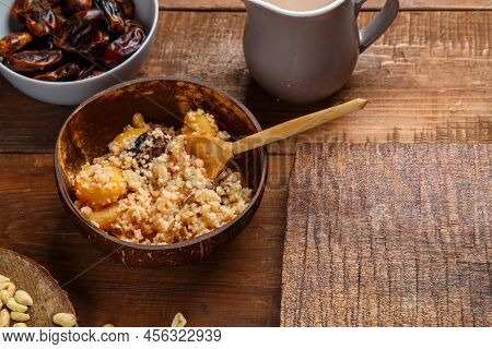 A Plate Of Couscous With Saffron And Nuts On A Wooden Table Next To Dates And A Jug Of Fruit Broth. 