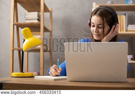 Girl Speaking In Headphones And Writing At Notebook. Student Woman Online Larning