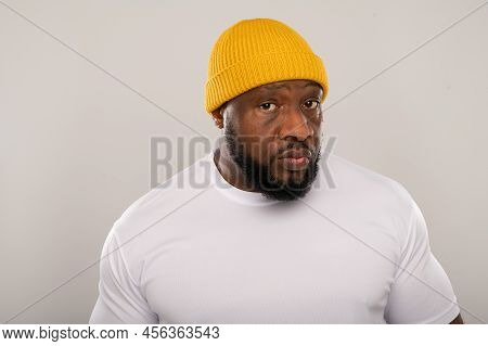 Muscular Nigerian man with a beard wearing a white sweat shirt and a yellow beanie hat on a light background with copy space