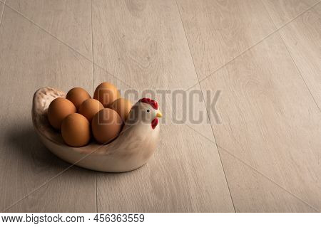 Chicken Eggs In Shells In A Chicken Shaped Dish On A Plain Light Wood Background With Copy Space