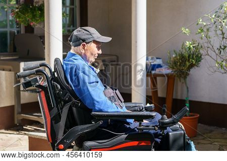 Lonely Senior Old Man In A Wheelchair Is Sitting Igarden Or Park. From Back Without Recognizable Fac