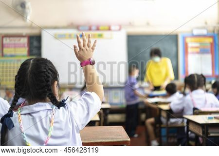One Elementary School Student Is Raising Their Hands To Ask The Teacher Standing In Front Of The Cla