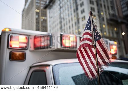 Close-up Of American Flag Against Red Flasher Light Of Siren Of Ambulance Car. Themes Emergency, Res