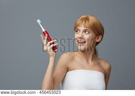 Nice Woman In A Canvas With Light Clean Skin, With Red Silky Hair Gathered In A Ponytail On A Gray B