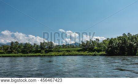 A Calm Blue River. There Is Lush Green Vegetation On The Shore. Mountains On The Background Of Azure