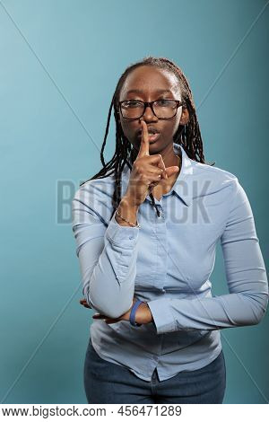 Attractive Serious Woman Making Silence Gesture By Putting Forefinger Over Lips On Blue Background. 