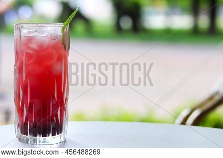 Icy Cherry Drink In A Glass With Mint And Ice On The Terrace. Thirst Quencher Concept. Selective Foc