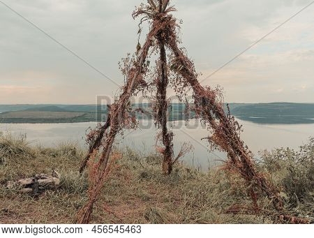 A Tent Made Of Twigs On The Banks Of A Large River. A Smooth Calm Water View.