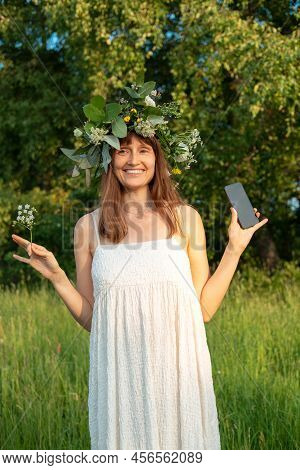 Woman With Flower Wreath At Midsummer Festival. Holding Phone For Shooting.