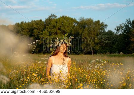 Woman With A Flower Wreath On Her Head Sits In A Field And Enjoys The Sun.