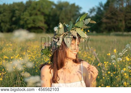 Woman With A Flower Wreath On Her Head And Blows On A Dandelion.