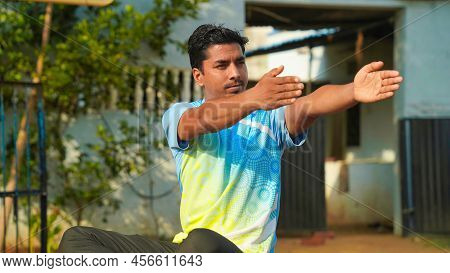 Good Looking Man In Blue Sport Shirt And Black Pants Sitting On Yoga Mat Doing Maditation With Hand