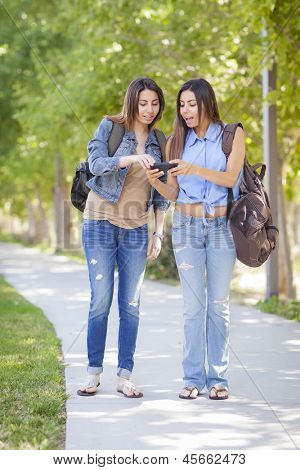 Jovem adulto misturado irmãs gêmeas de corrida partilha experiência de telefone celular fora.