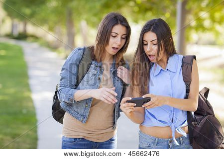 Jovem adulto misturado irmãs gêmeas de corrida partilha experiência de telefone celular fora.
