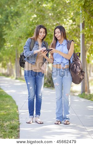Jovem adulto misturado irmãs gêmeas de corrida partilha experiência de telefone celular fora.