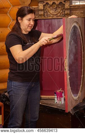 Woman With Brush Looking At Door Of Antique Cupboard With Beautiful Ornaments And Painting It. Re-us