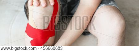A Man Sits With A Kinesiology Tape On His Knee, Legs Close Up. Supports Knee Muscles. Ligament Sprai