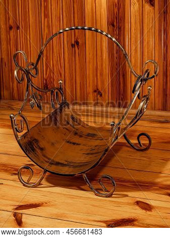 Antique empty metal firewood basket by a wooden wall