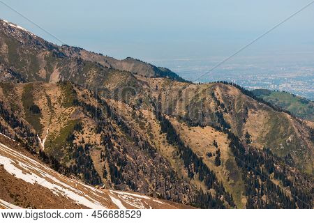 Rocky Snow-capped Mountains Under The Sun And Blue Sky, Behind Them The City