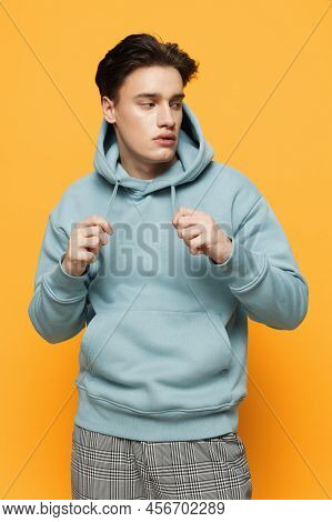 A Handsome Teenager Stands On An Orange Background In A Light Hoodie And Pulls Aside The Lacing