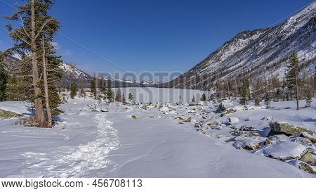 Picturesque Boulders Are Scattered In The Snow-covered Valley, Coniferous Trees Grow. The Path Is Tr