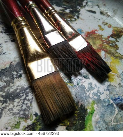 Artists Brushes Or Painting Brushes With Palatte And Colour Bottles In Blurred Background.