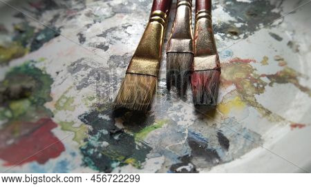 Artists Brushes Or Painting Brushes With Palatte And Colour Bottles In Blurred Background.