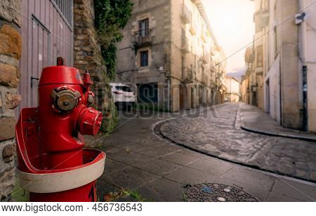 Red Fire Hydrant On Sidewalk In Onati City, Spain. Fire Hydrant On Blur Old Building, White Car, And