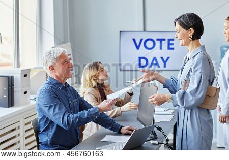 Side View Portrait Of Smiling Adult Woman Taking Ballot Form While Voting On Election Day, Copy Spac