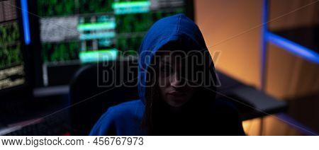 Hooded Anonymous Hacker By Computer In The Dark Room At Night, Cyberwar Concept.