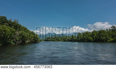 The Bed Of The Blue River Bends Along The Green Banks. Ripples On The Water. Mountains Against The S