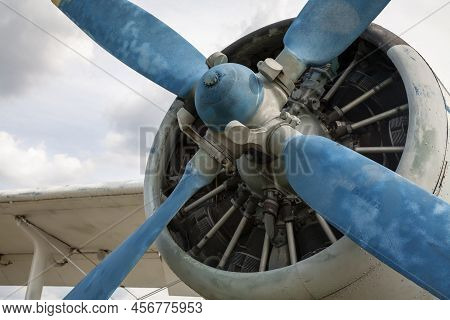 Vintage Airplane Fragment With Blue Propeller, Motor Details And Wing With Cloudy Sky On The Backgro