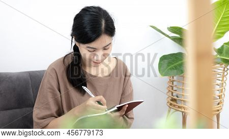 Asian woman sits in her living room writing a diary or notebook on the carpet, Weekends or holidays 