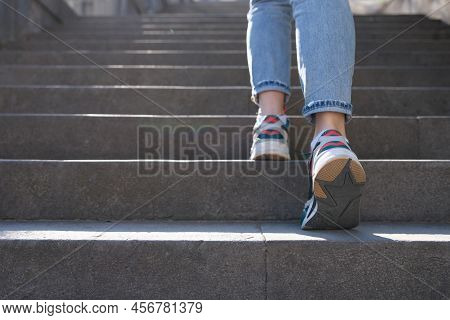 Close-up Of Female In Jeans And Sneakers Going Up Steep Stairs. Woman Tourist In Casual Clothes Goin
