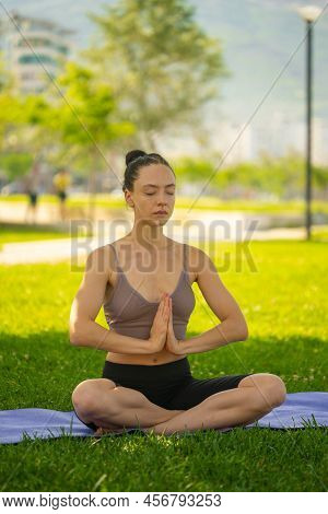 A Woman In Brown Sport Bra And Black Short Sitting On Yoga Mat Doing Maditation With Hand Together A