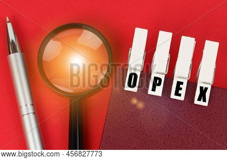 Business Concept. On The Red Surface There Is A Magnifying Glass, A Notepad And Clothespins With The