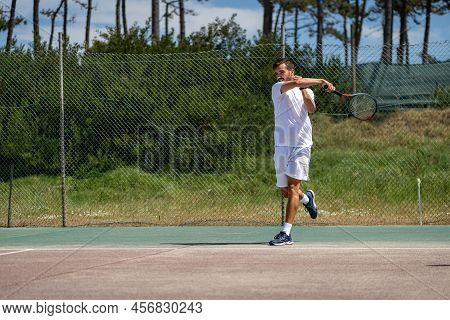 Tennis Player Hitting Forehand At Ball With Racket On Court.