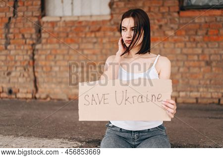 Women With Poster Save Ukraine. A Woman With A Belligerent Look Looks To The Side. Wind Develops Hai